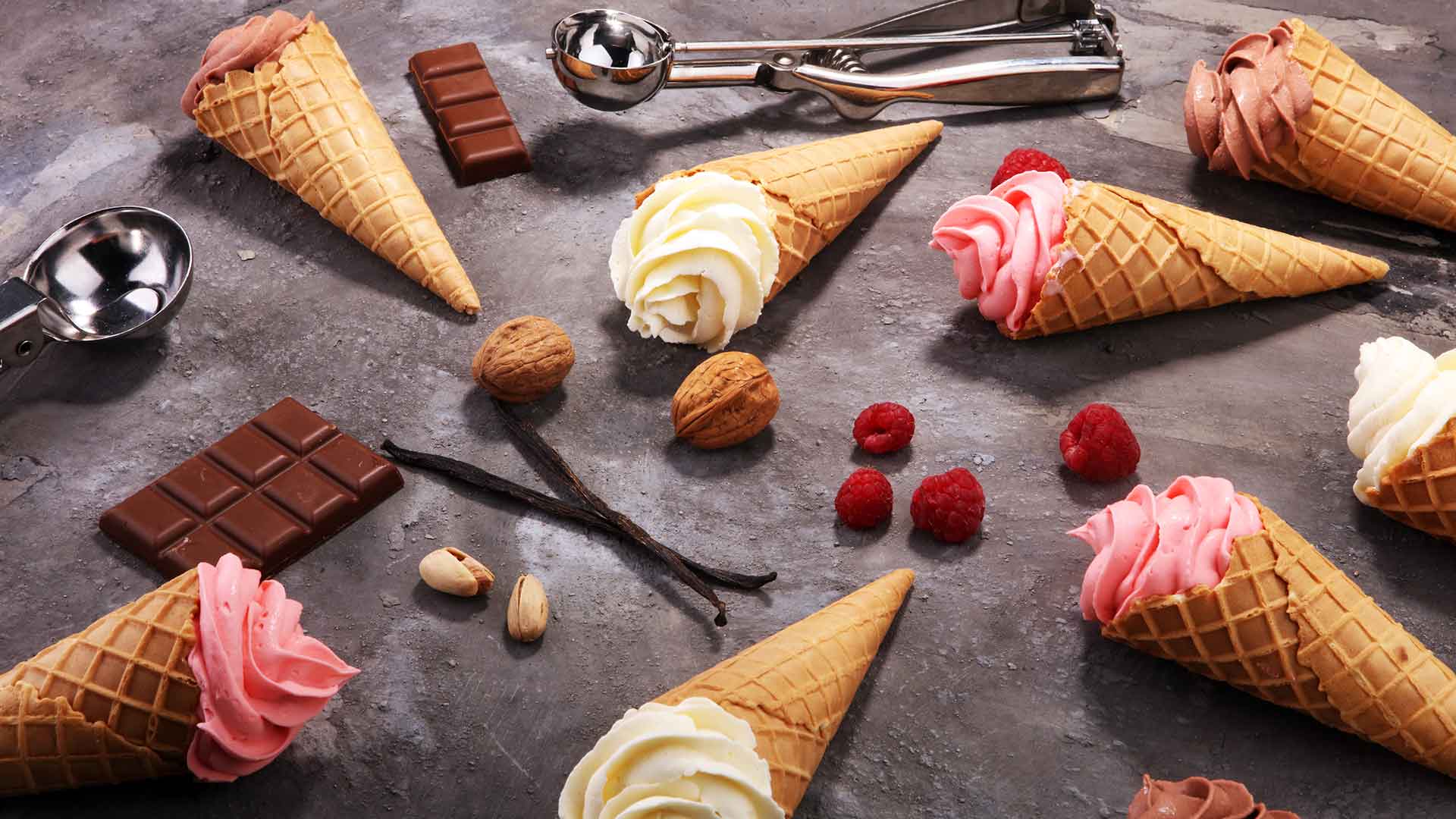 Ice cream cones with different flavors on a dark surface with chocolate bars and berries.