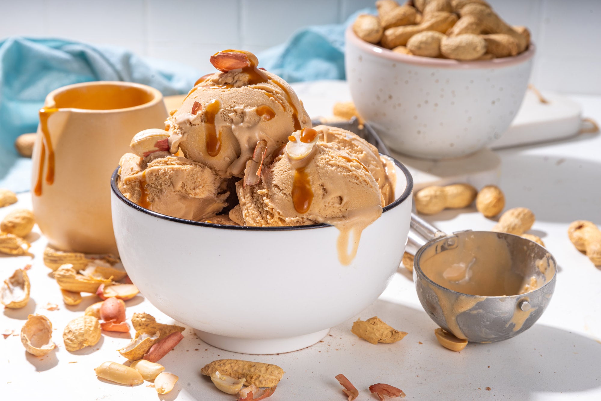 Bowl of peanut butter ice cream with peanuts and a measuring cup on a light surface.